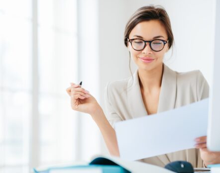 Concentrated successful businesswoman looks attentively in paper, studies terms of contract